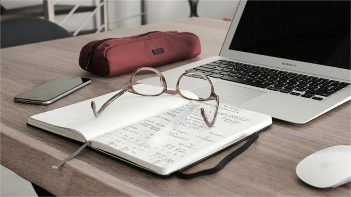 Notebook with glasses beside a laptop on a desk